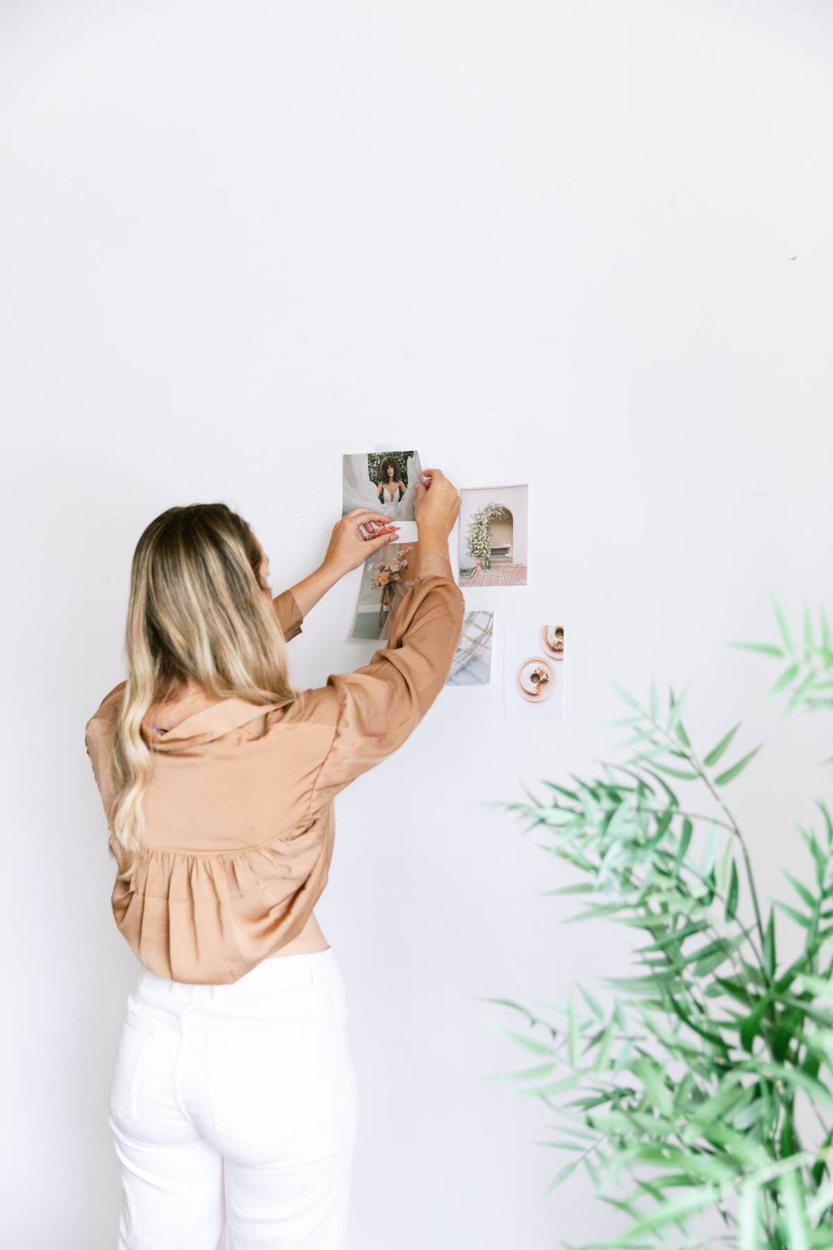 blonde woman working on a collage of images on a white wall